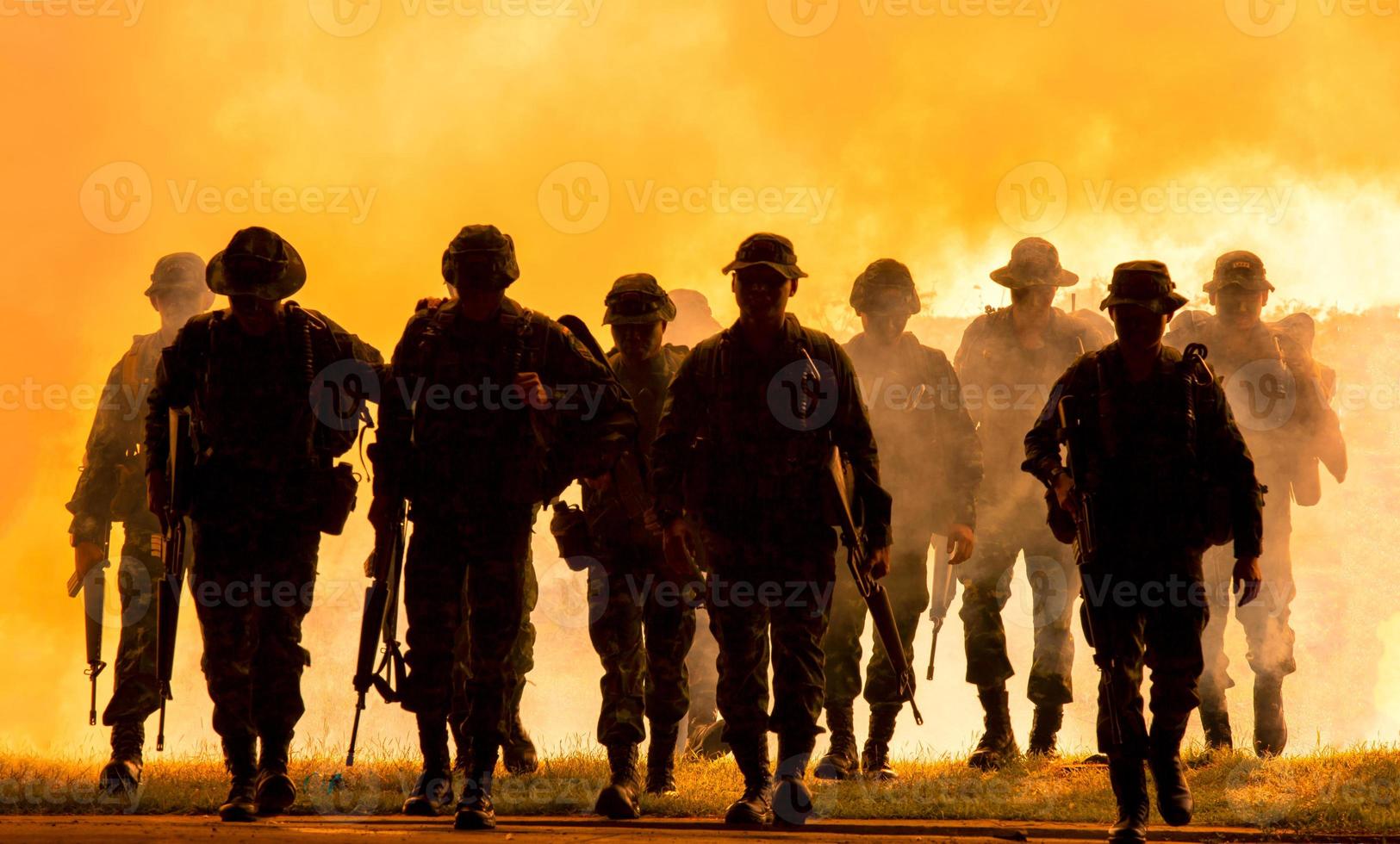 siluetas de soldados del ejército en la niebla contra una puesta de sol, equipo de marines en acción, rodeado de fuego y humo, disparando con rifle de asalto y ametralladora, atacando al enemigo foto