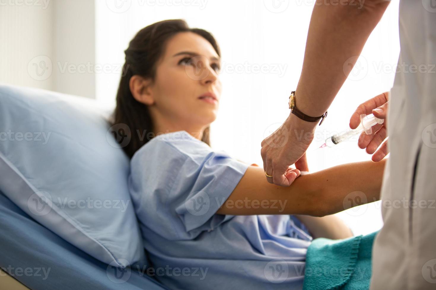 Portrait of young female patient lying on clinic bed wearing hospital gown. photo