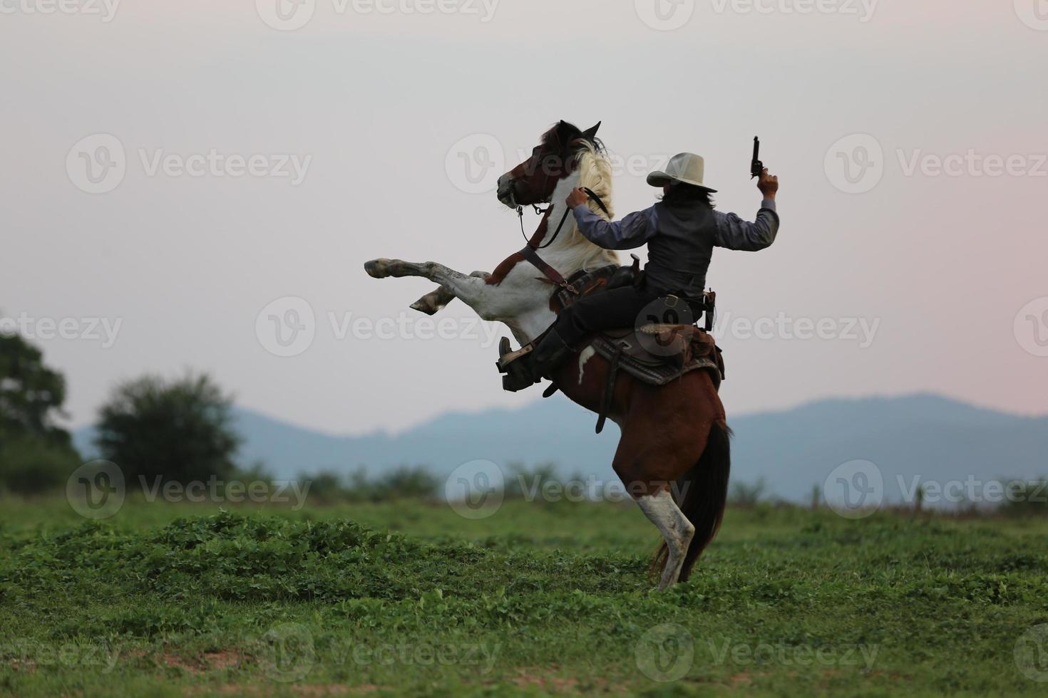 Cowboy riding horse with hand holding gun against sunset background. photo