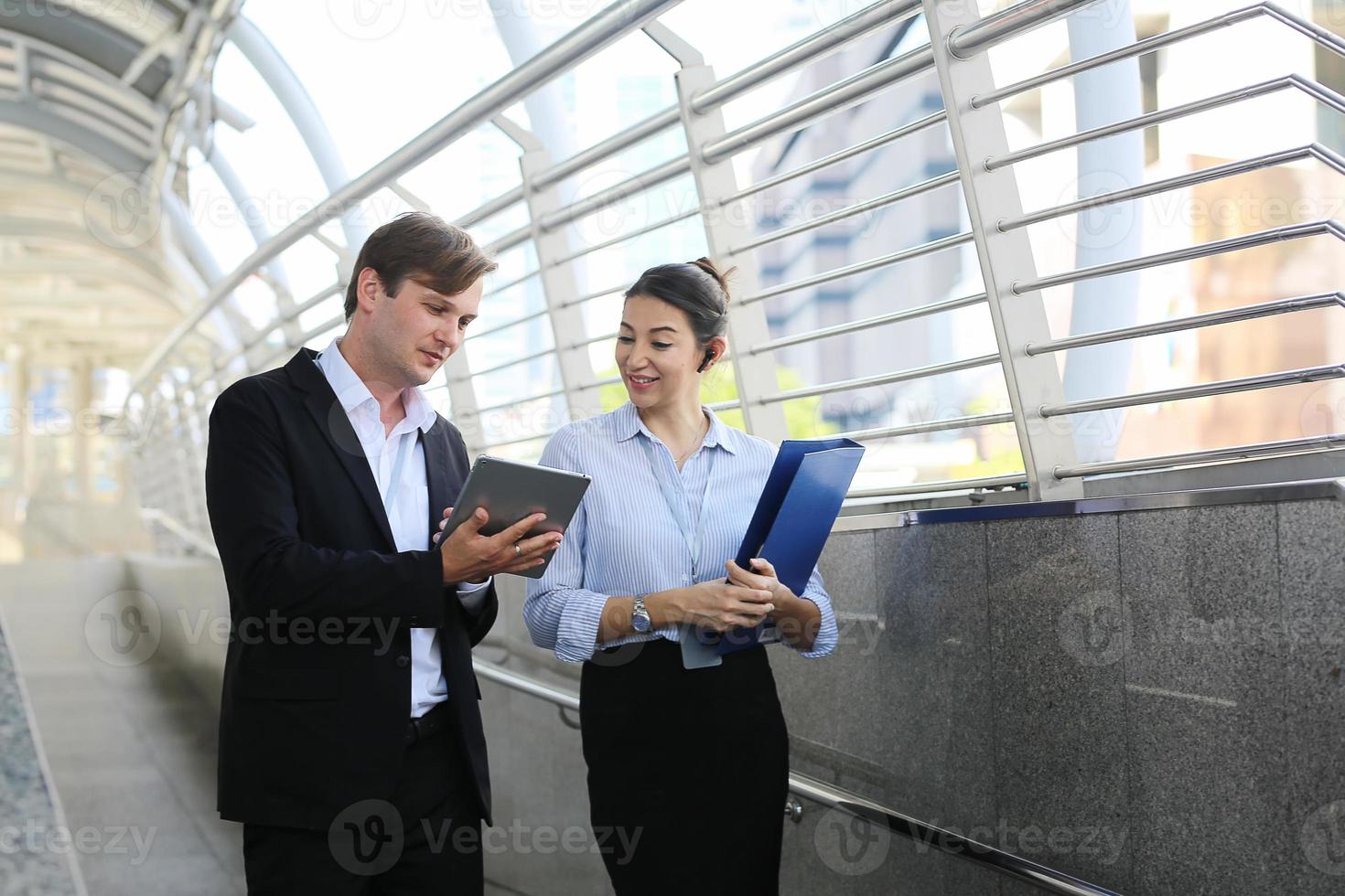 businessman showing content on tablet to female colleague. Business man and woman walking outside, using tablet, talking, smiling, laughing. Communication concept photo