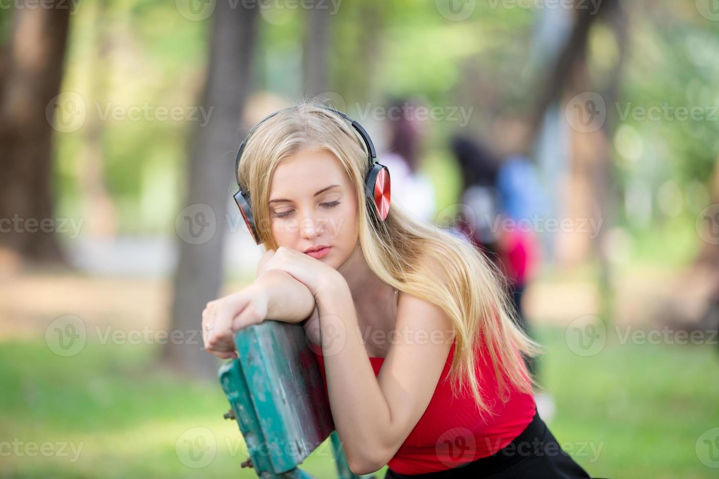 Beautiful blonde woman standing while listening music on headphone at park. photo