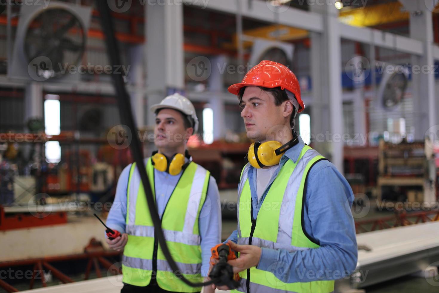 Men industrial engineer wearing a safety helmet while standing in a heavy industrial factory. The Maintenance looking of working at industrial machinery and check security system setup in factory. photo