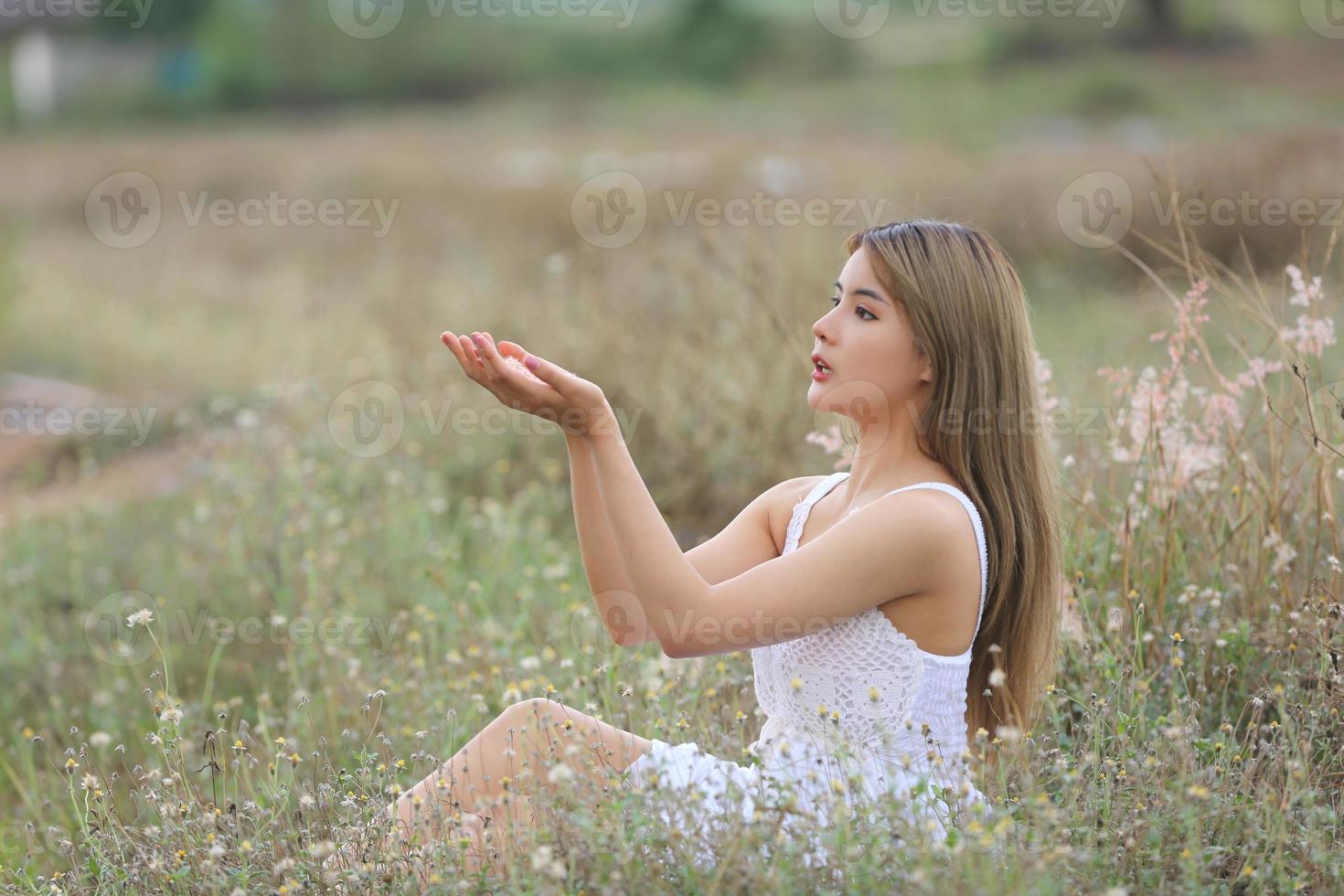 Beautiful Young Woman sitting on the field in green grass and blowing dandelion. Outdoors. Enjoy Nature. Healthy Smiling Girl on spring lawn. Allergy free concept. Freedom photo