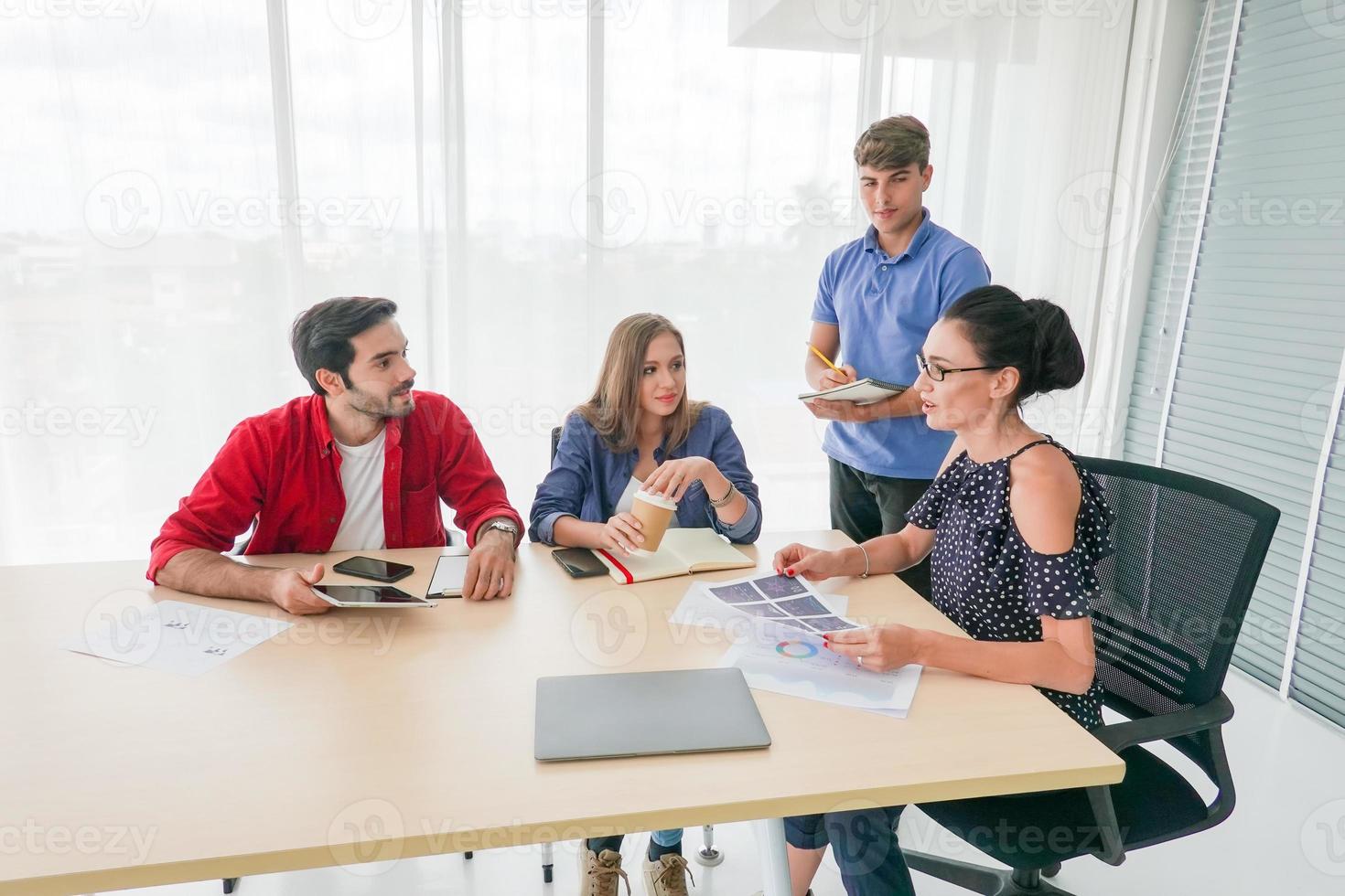 grupo diverso de jóvenes empresarios discutiendo un proyecto de trabajo mientras se sientan juntos en una mesa en una oficina moderna. concepto de coworking foto