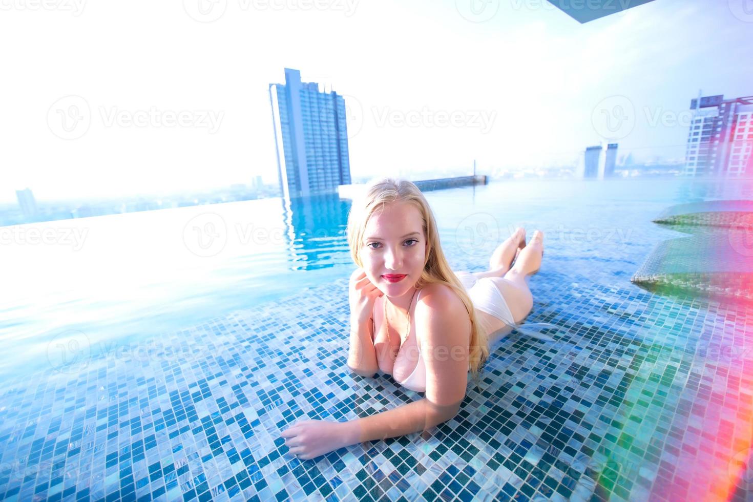 mujer joven disfrutando de un sol, modelo de niña delgada en bikini blanco junto a la piscina. foto