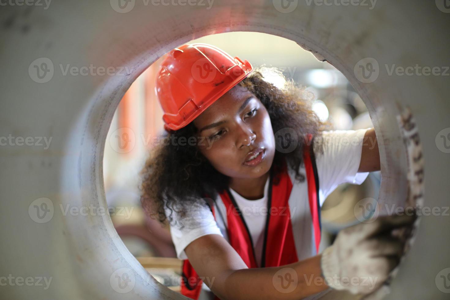 Female industrial engineer wearing a safety helmet while standing in a heavy industrial factory. The Maintenance looking of working at industrial machinery and check security system setup in factory. photo