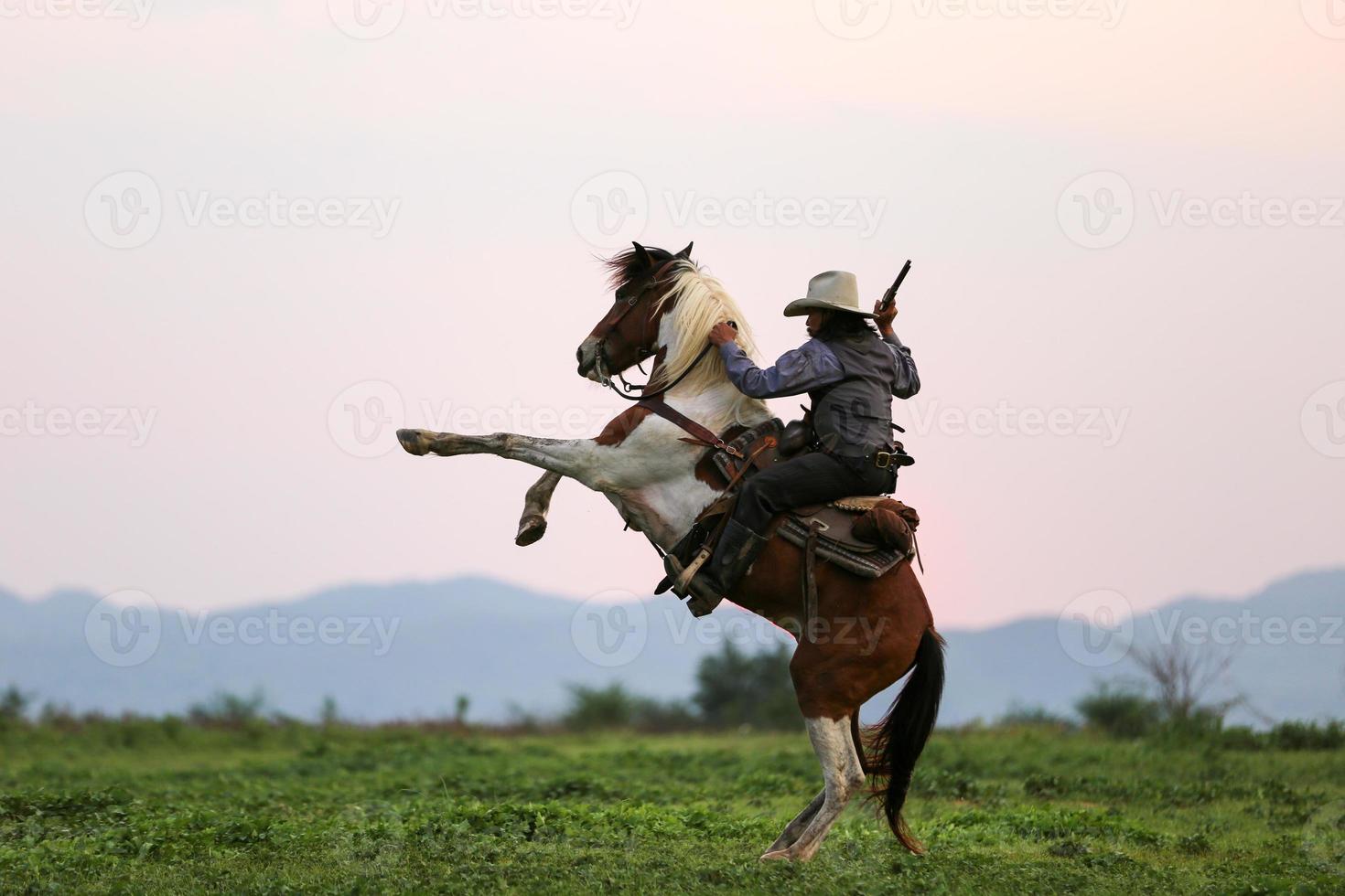 Cowboy riding horse with hand holding gun, Cowboy on horseback against a beautiful sunset, cowboy and horse at first light, mountain, river and lifestyle with natural light background photo