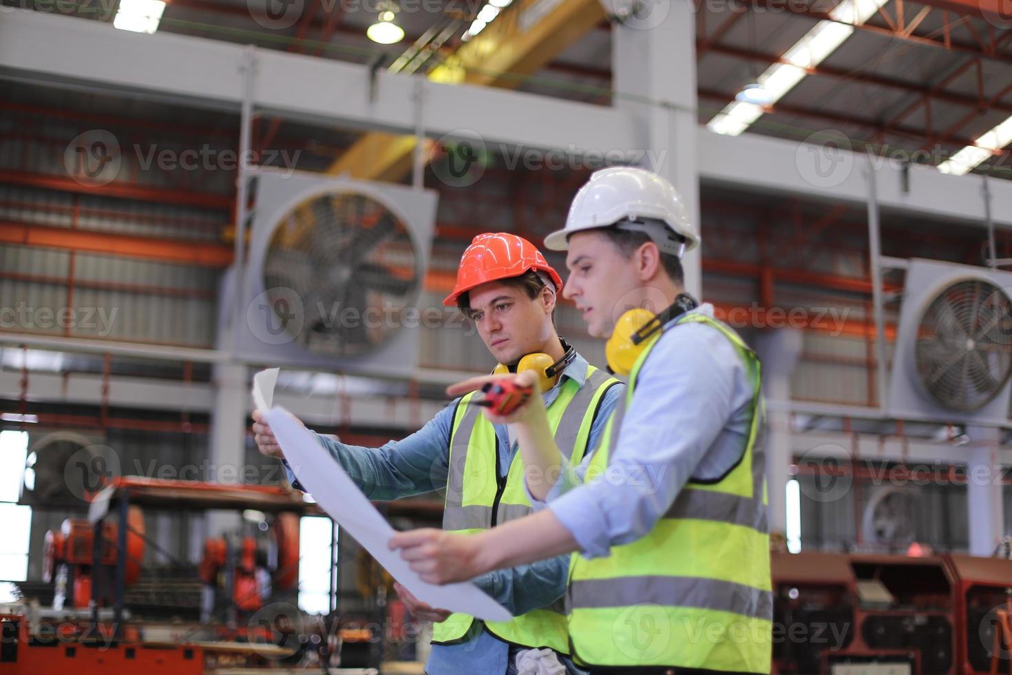 Men industrial engineer wearing a safety helmet while standing in a heavy industrial factory. The Maintenance looking of working at industrial machinery and check security system setup in factory. photo