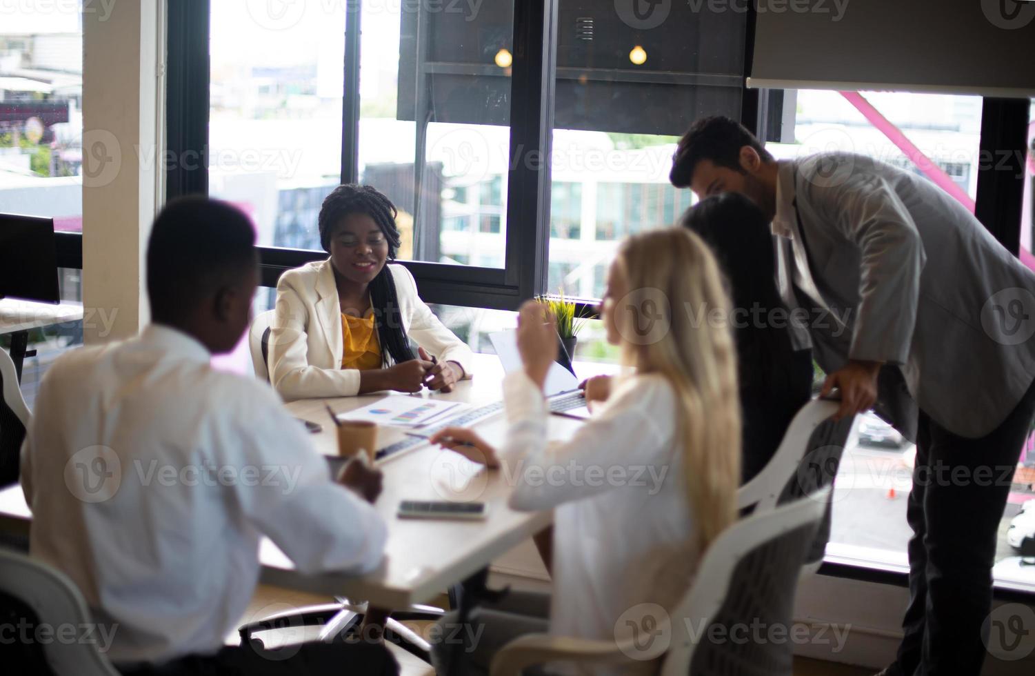 diversos colegas de negocios sentados en un escritorio en una oficina moderna hablando juntos sobre una computadora portátil foto