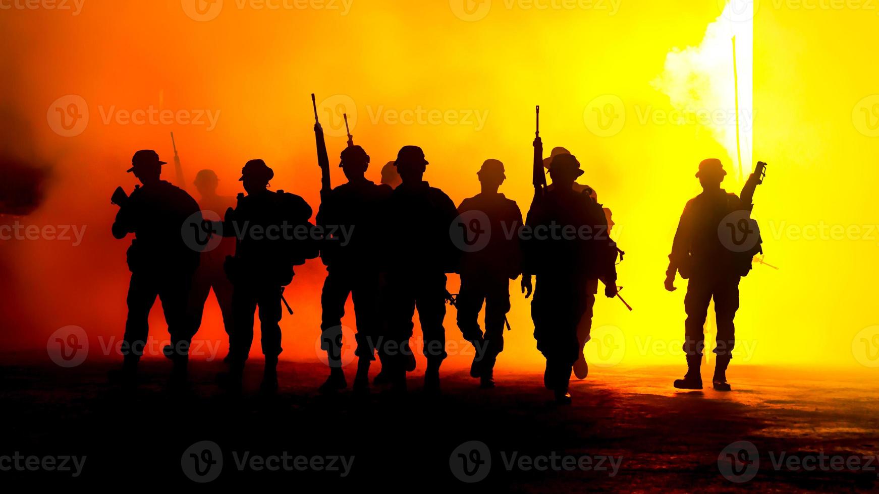 siluetas de soldados del ejército en la niebla contra una puesta de sol, equipo de marines en acción, rodeado de fuego y humo, disparando con rifle de asalto y ametralladora, atacando al enemigo foto