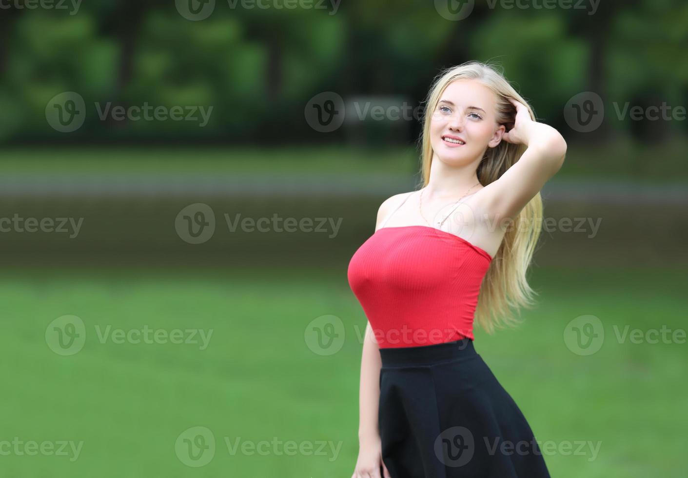 hermosa mujer rubia de pie mientras escucha música en los auriculares en el parque. foto