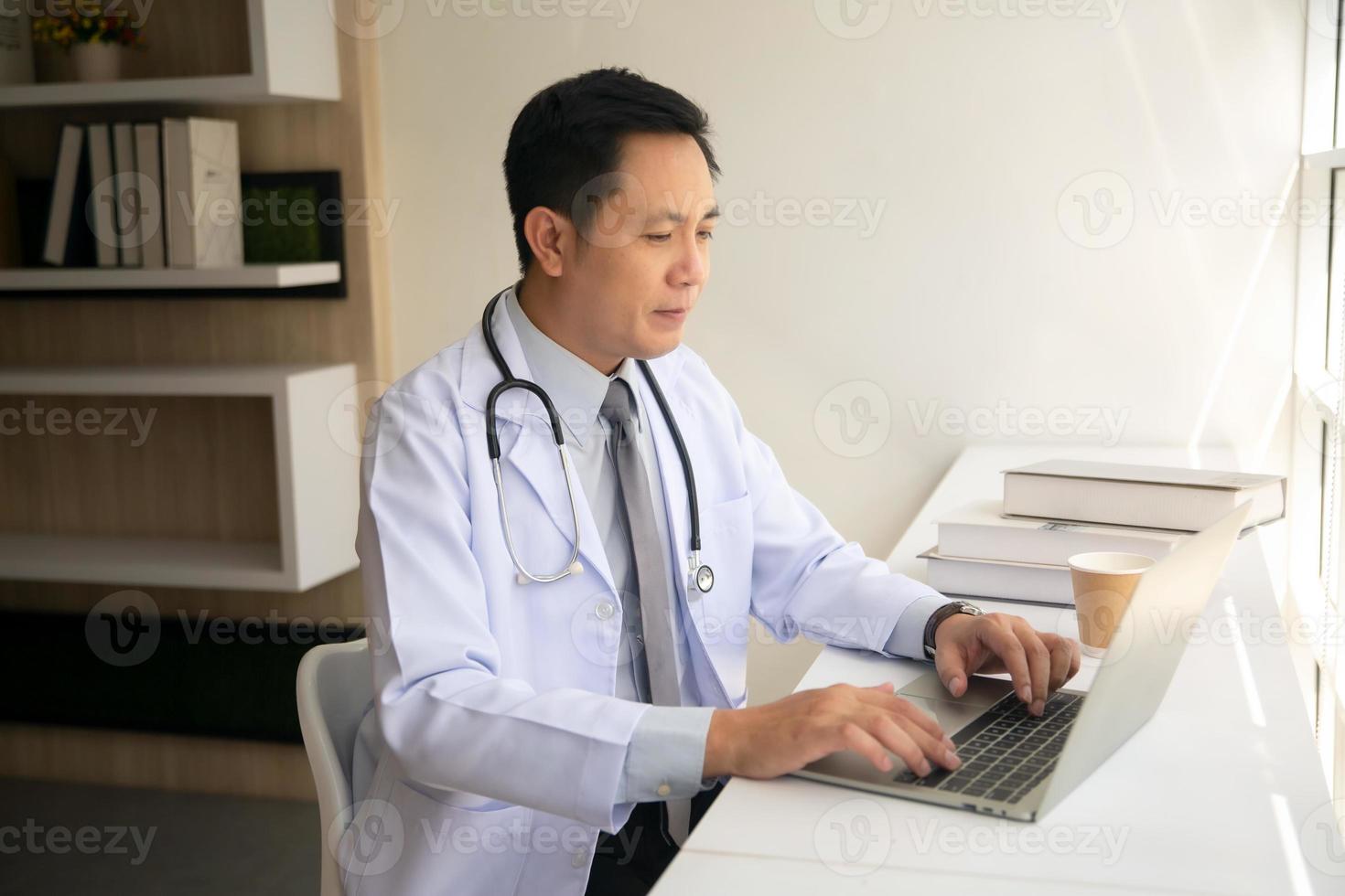 Asian male Doctor using laptop by window in his office. photo