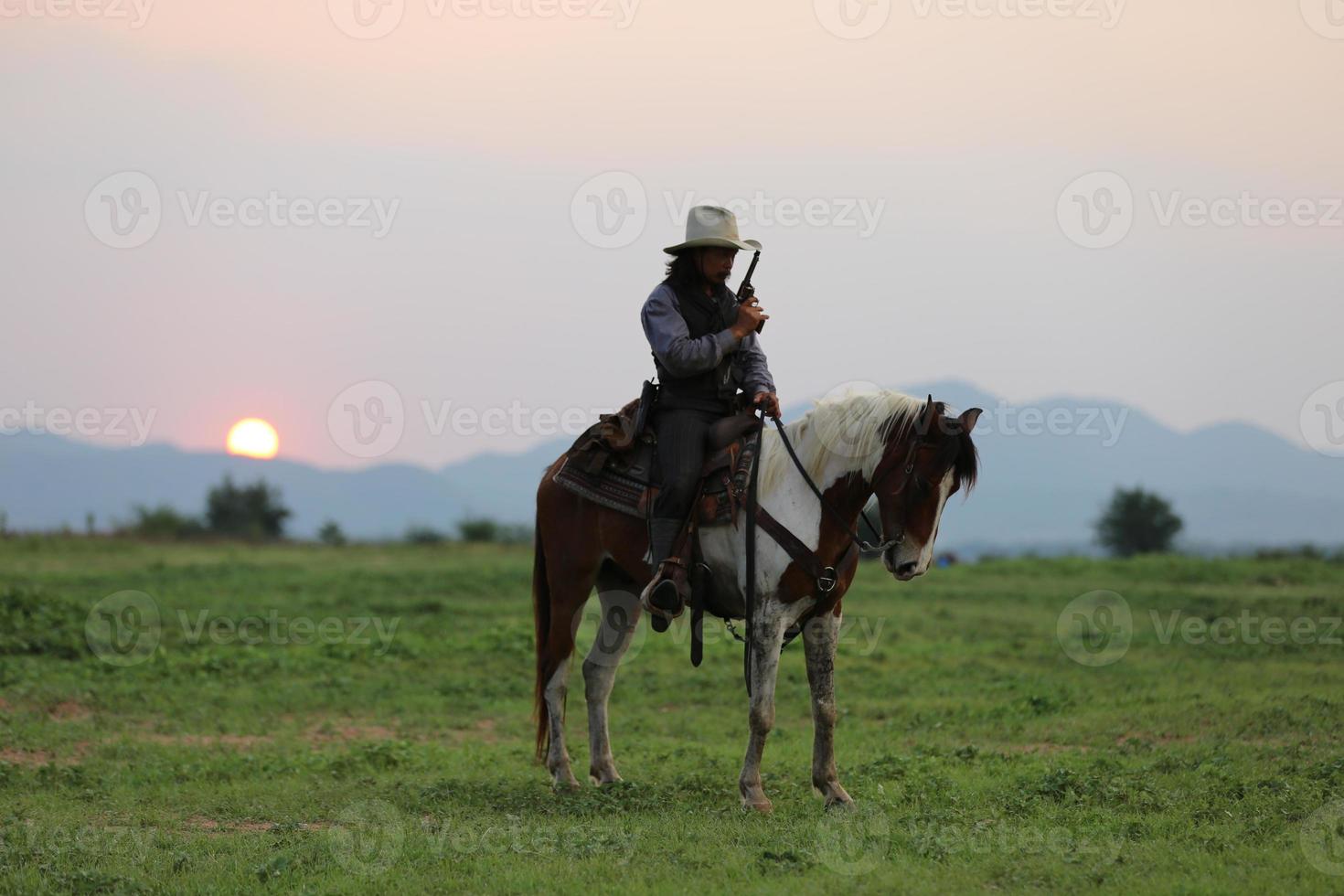 vaquero montando a caballo con la mano sosteniendo un arma contra el fondo del atardecer. foto