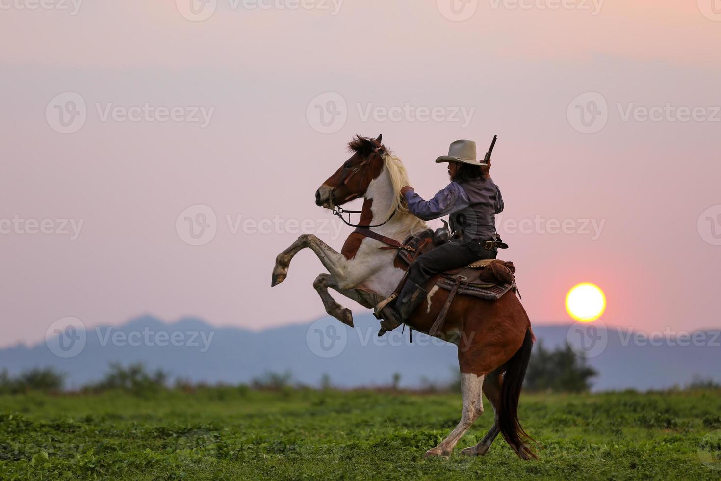 vaquero montando a caballo con pistola de mano, vaquero a caballo contra una hermosa puesta de sol, vaquero y caballo a primera luz, montaña, río y estilo de vida con fondo de luz natural foto
