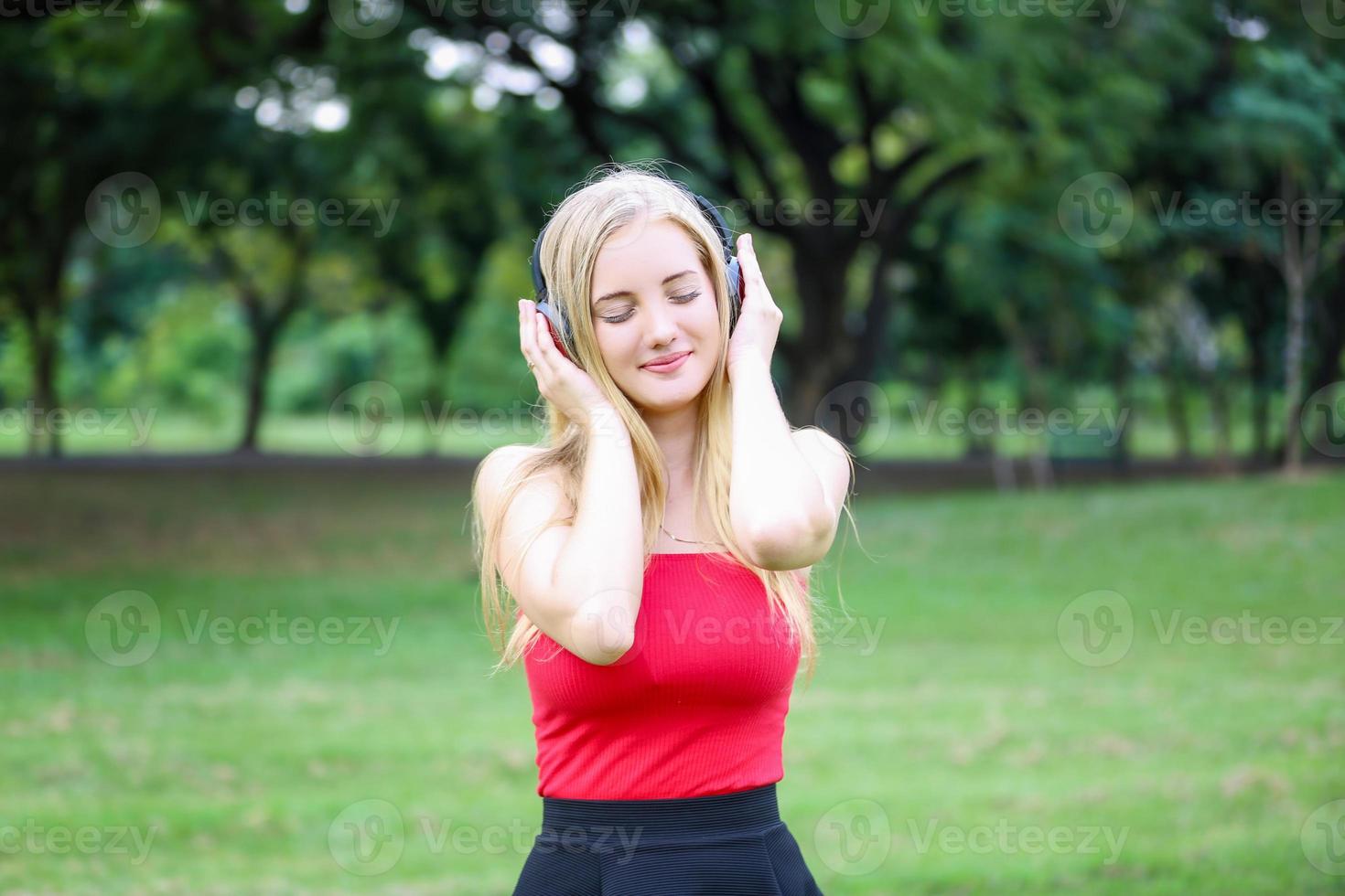 hermosa mujer rubia de pie mientras escucha música en los auriculares en el parque. foto