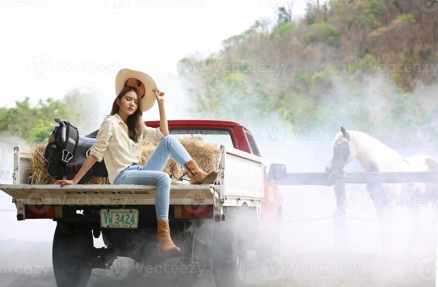 Cowgirl model posing on farm. A portrait of a beautiful young cowgirl leaning against a wall in a stable at farm. photo