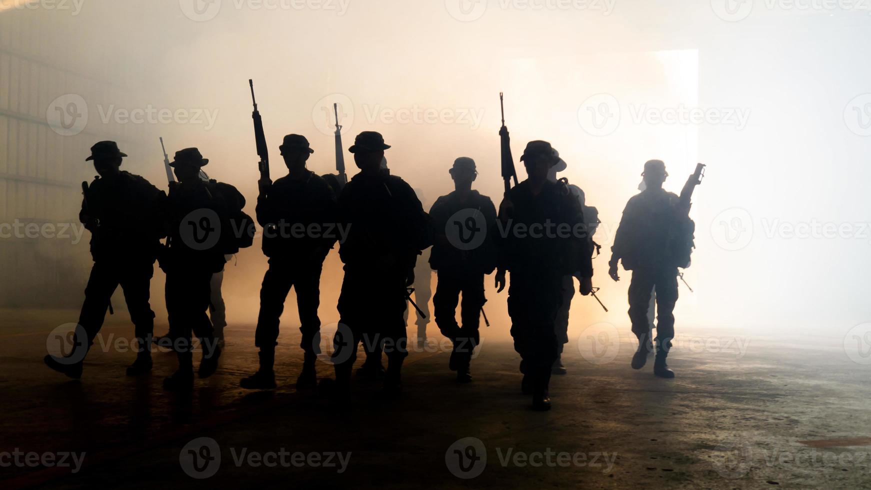 siluetas de soldados del ejército en la niebla contra una puesta de sol, equipo de marines en acción, rodeado de fuego y humo, disparando con rifle de asalto y ametralladora, atacando al enemigo foto