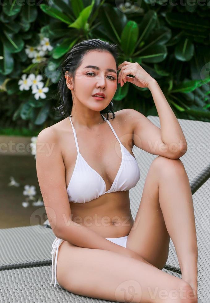 Young woman enjoying and relaxing at poolside. Slim young girl model in white bikini  by the pool. photo