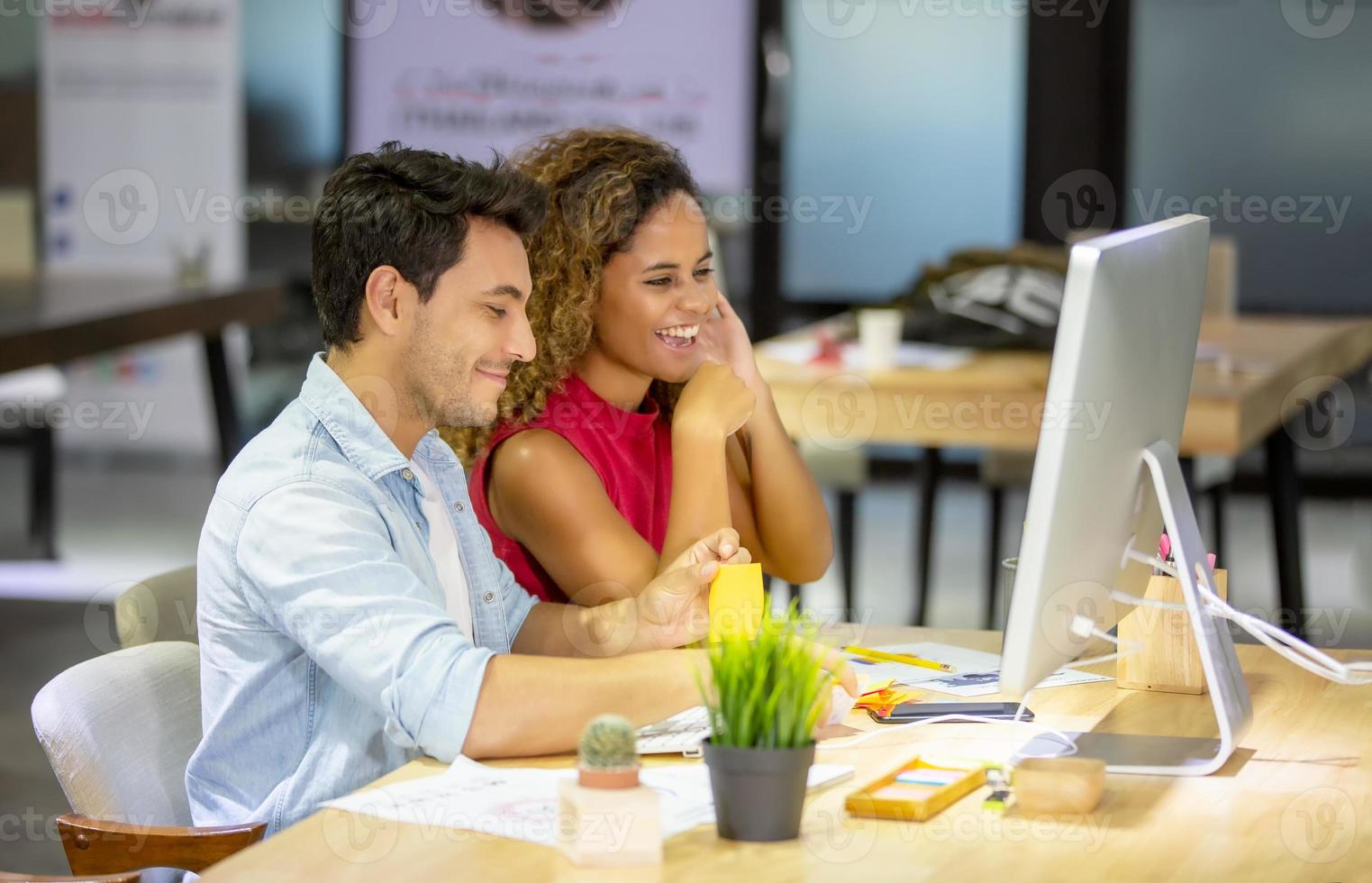 Diverse business colleagues sitting at a desk in a modern office talking together over a computer. photo