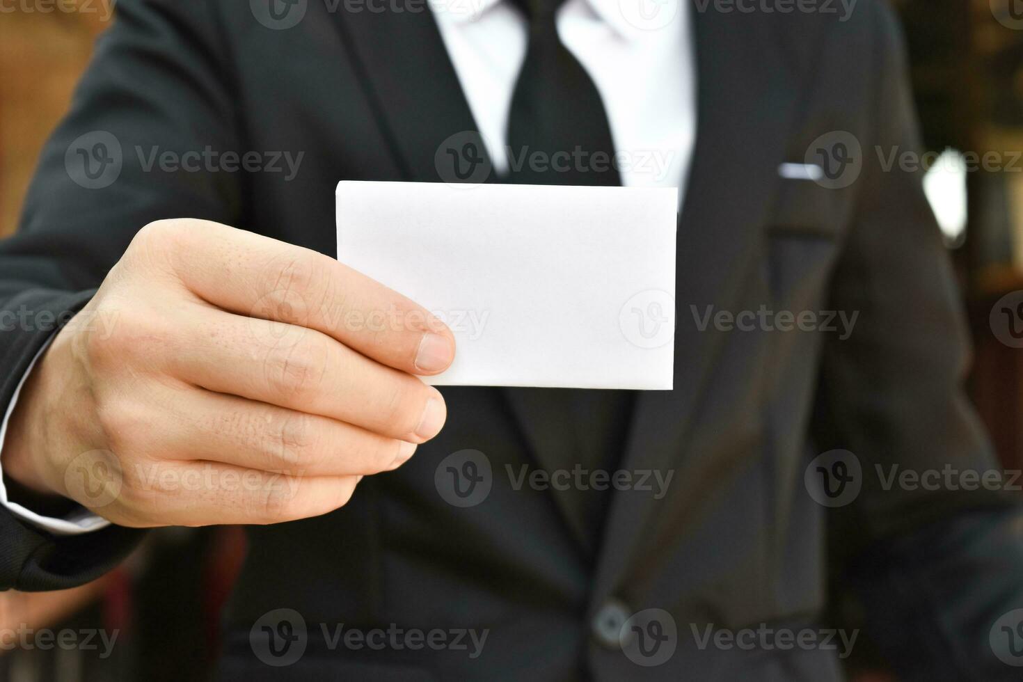 Closeup of businessman showing white piece of paper in black suit. Idea for business credit card or visiting card. photo