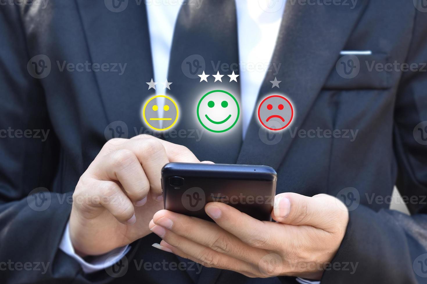 Businessman pressing face emoticon in smartphone at display on virtual screen. Concept of customer service satisfaction evaluation and feedback. photo