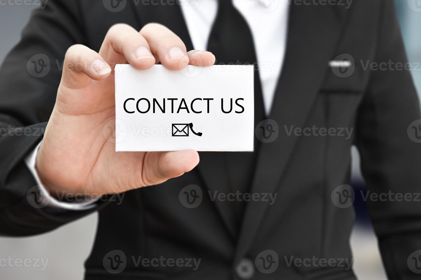 Businessman hand holding business card with the message contact us. Idea for customer support hotline people connect photo