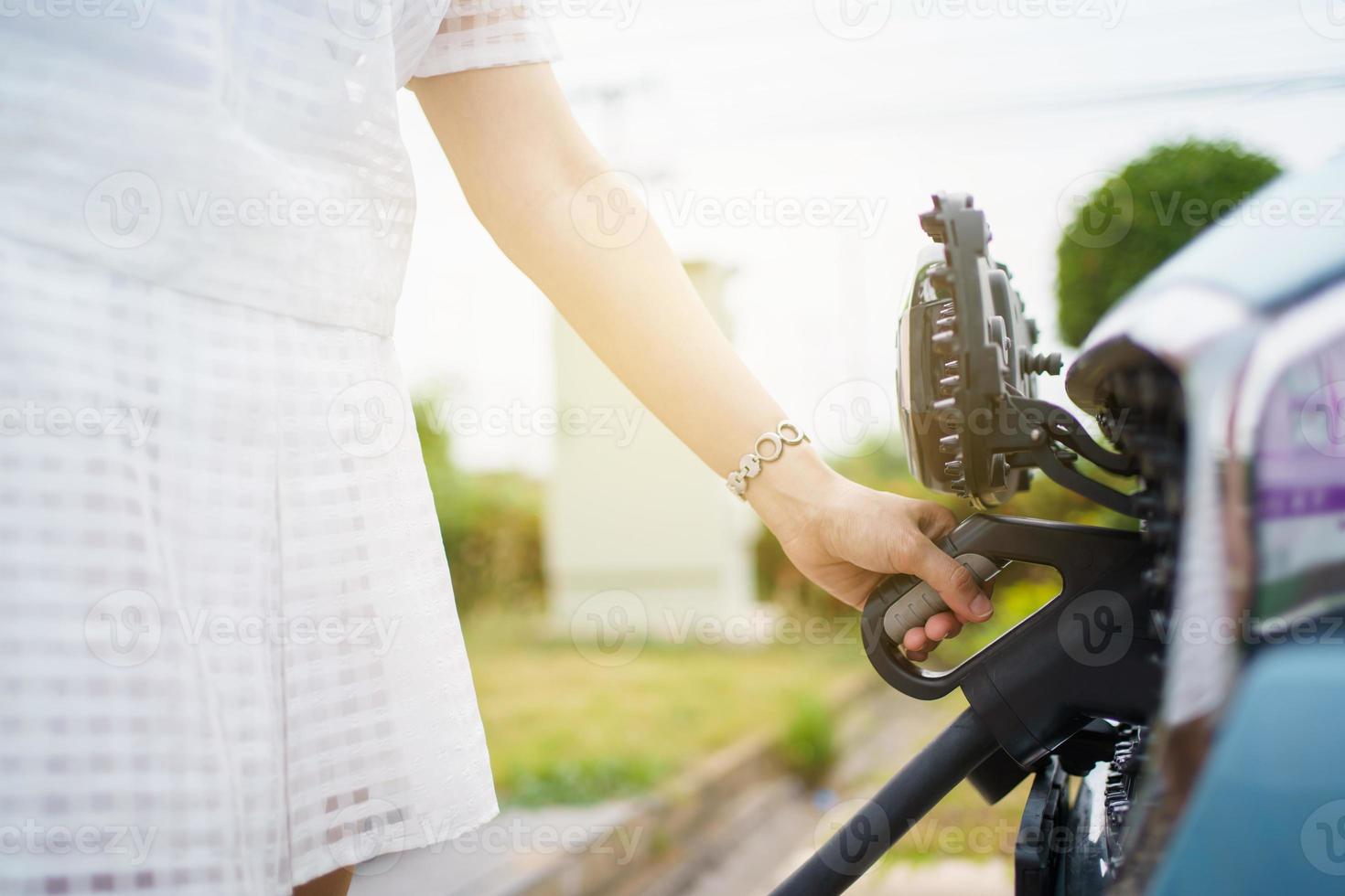Asian woman holding AC type 2 EV charging connector at EV charging station, woman preparing an EV - electric vehicle charging connector for recharge a vehicle. photo