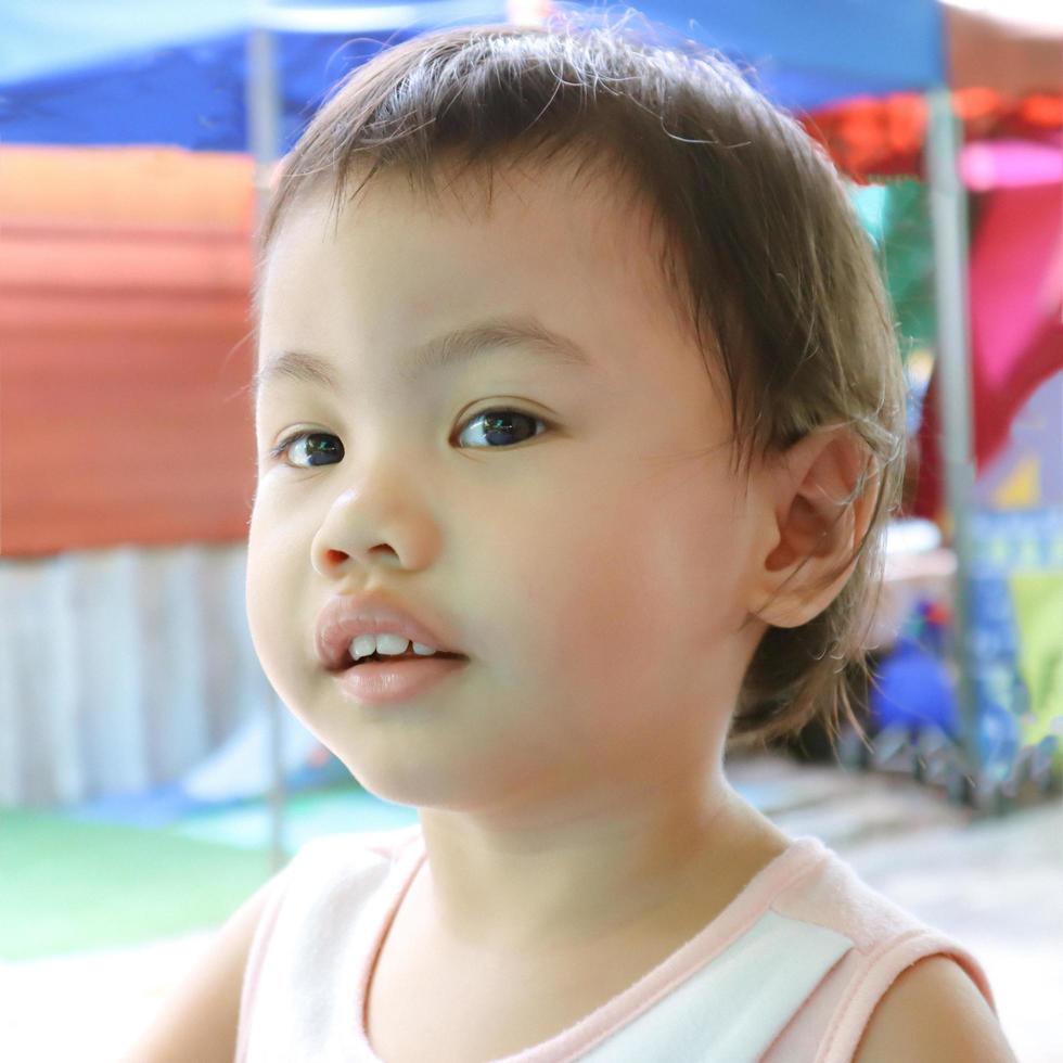 Linda niña asiática de 3 años, pequeña niña pequeña mirando a la izquierda con cara sonriente. foto