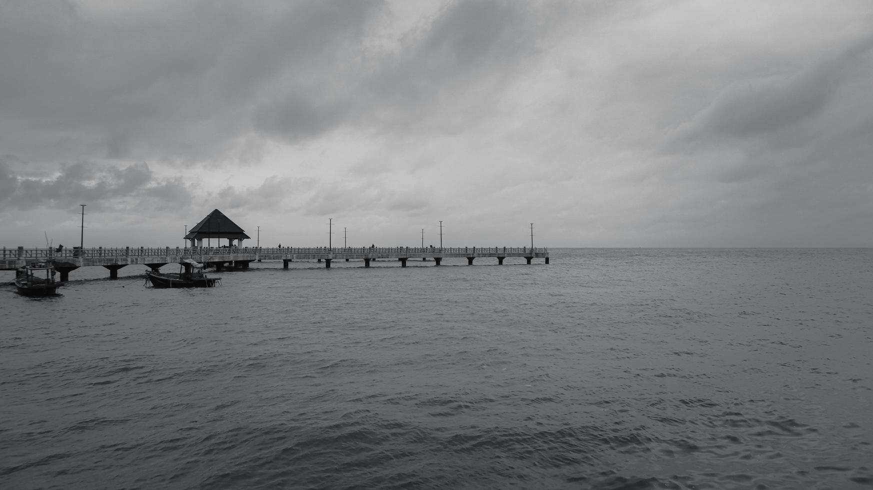 Black and white, fine art landscape photograph of a pier with dramatic sky at sea photo