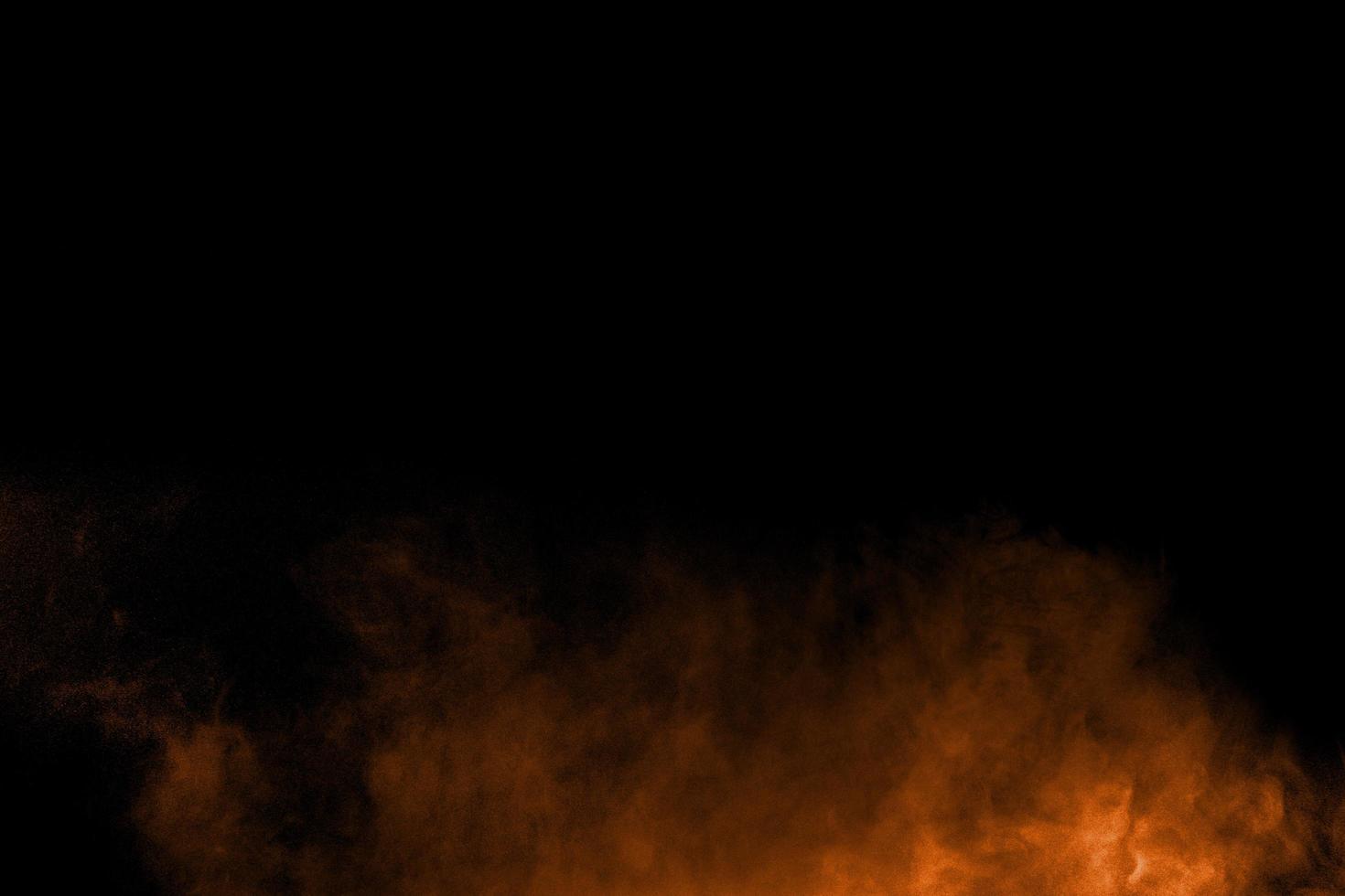 Abstract orange powder explosion on black  background. Freeze motion of orange  dust particles splash. photo