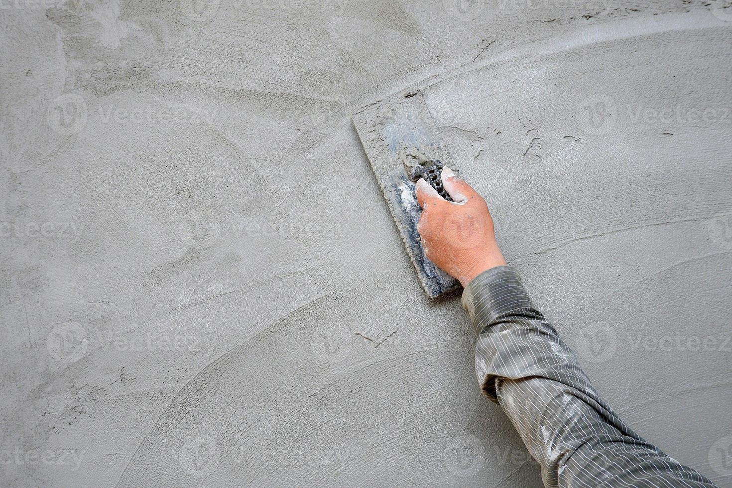 Plasterer man hand using trowel to plastering cement on concrete wall background in construction site photo