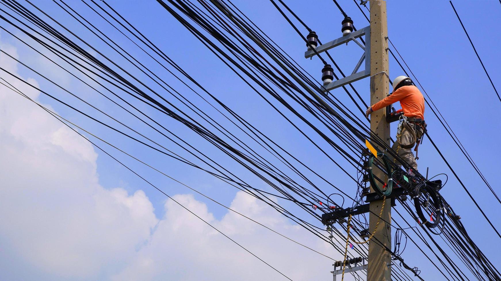 Low angle view of electrician lineman working to install electrical system on electric power pole against white cloud and blue sky background photo