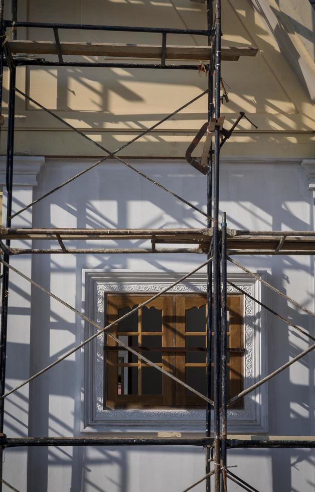 Sunlight and shadow on surface of the old scaffolding in front of wooden window on concrete wall of house building structure under renovate and construction in vertical frame, selective focus photo