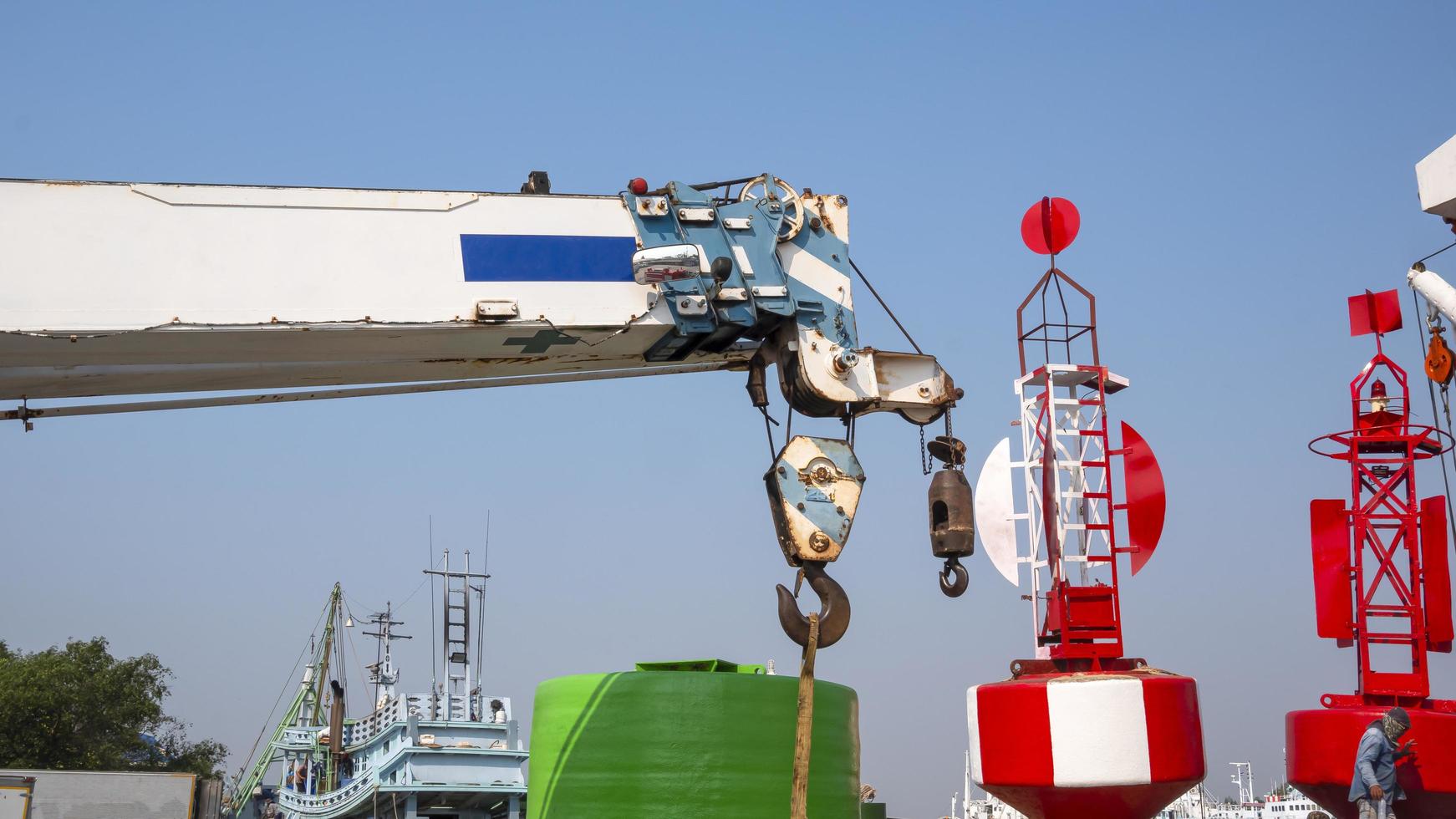 White crane boom and hoisting block, hook, steel wire rope with red fairway buoys against blue sky background at harbor photo