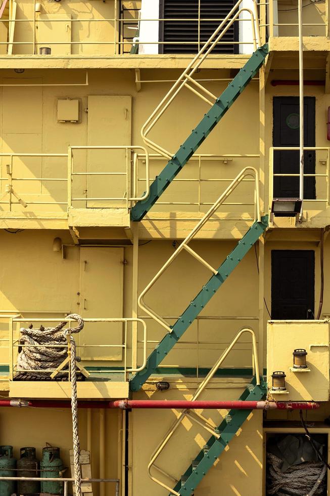 Part of green stairs up and down with railing on aft side of the old big yellow metal ship in vertical frame photo