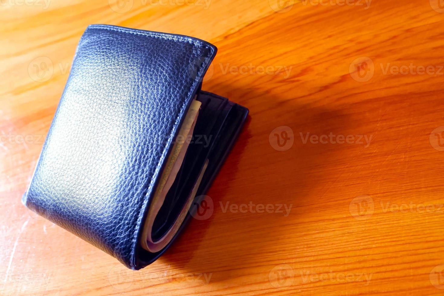 vista superior de la nueva cartera de cuero negro auténtico con billetes y tarjeta de crédito en el interior aislada sobre fondo de madera naranja. foto