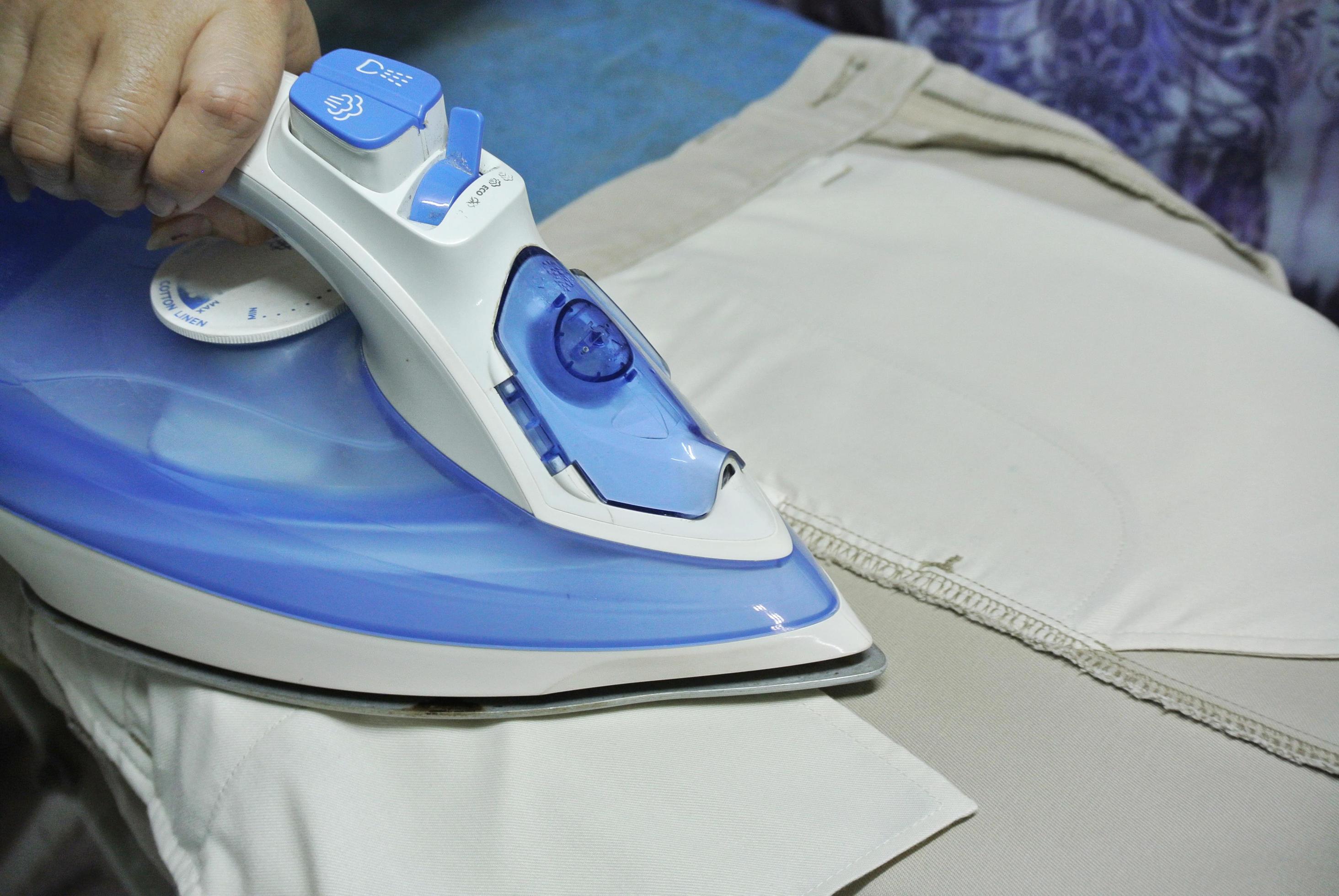 Women ironing trousers on ironing board in laundry room at home. The