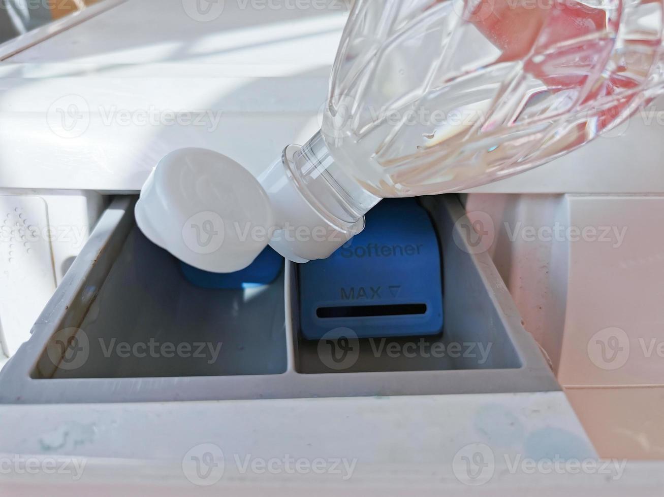 Close up hand pouring the vinegar into the front-loading drawer. Clean a washing machine with vinegar. photo