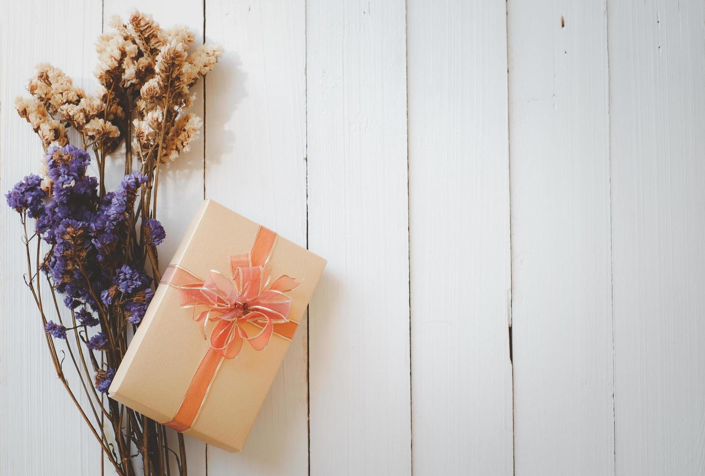 bunches of purple and white statice flower and gold gift box isolated on white wooden background with copy space for text. photo