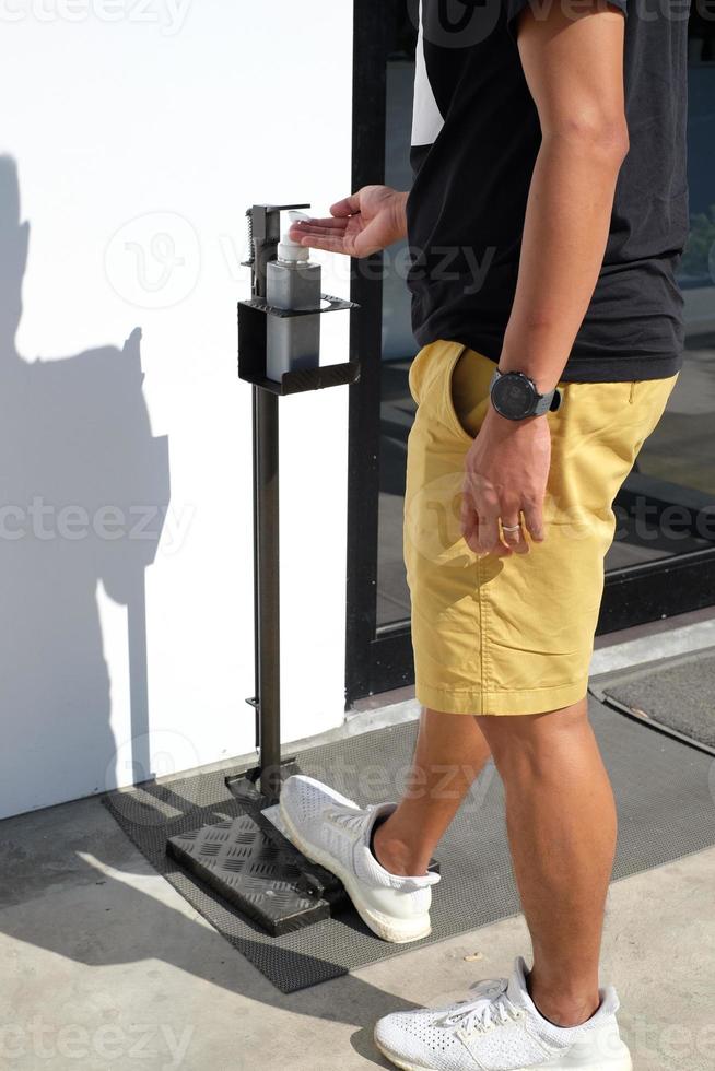 Close up picture of a man used foot operated hand sanitizer dispenser or hands free sanitizer stand at pubic area. Touchless equipment. cleaning and protect from Covid-19, Corona virus disease. photo