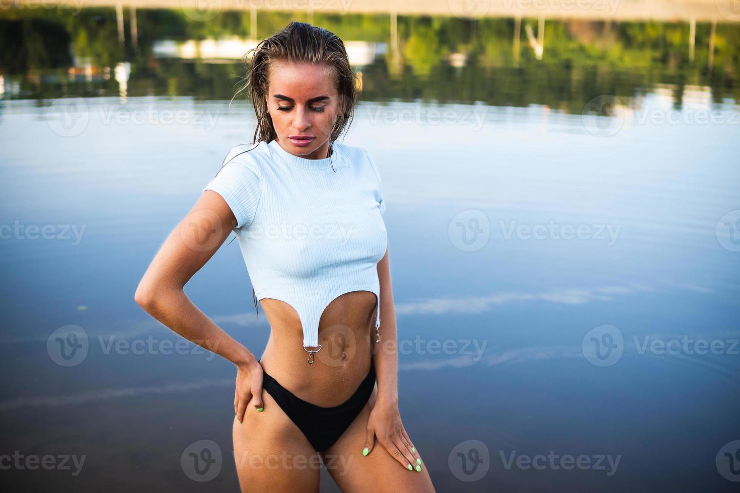 A beautiful brunette model in black panties and a T-shirt, posing in the water in front of the camera. photo