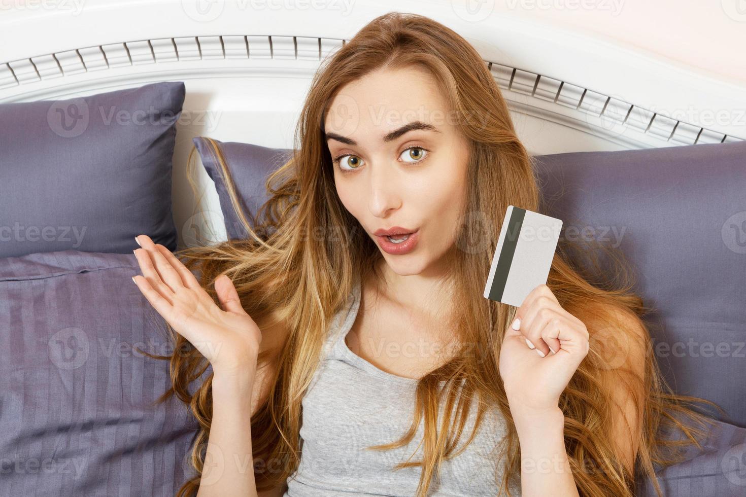 Smile emotional woman shopping on internet holding bank card and she lying on the bed at home. Asian girl buy online Using credit card she is in bed. photo