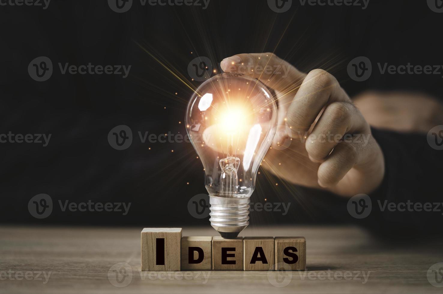 Businessman touching glowing light bulb on Idea wording print screen to wooden cube block for creative idea thinking and innovation concept. photo