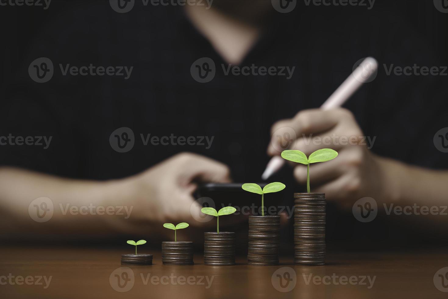 Plant growth on increasing coins stacking and businessman writing on smartphone for record and summary saving of growth profit and interest rating from investment concept. photo