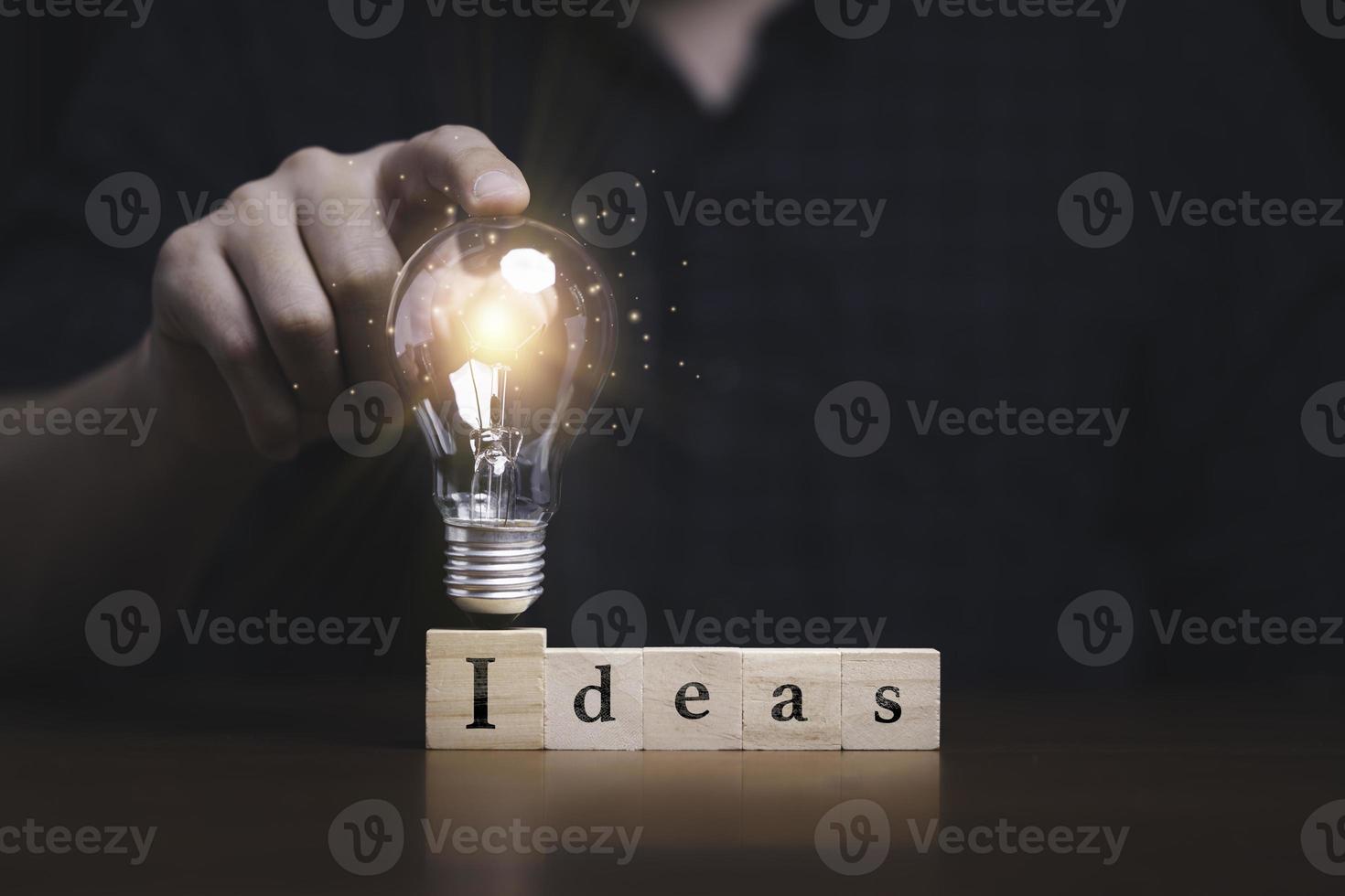 Hand touching to glowing lightbulb on ideas wording which print screen on wooden cube block for creative thinking idea and problem solving concept photo