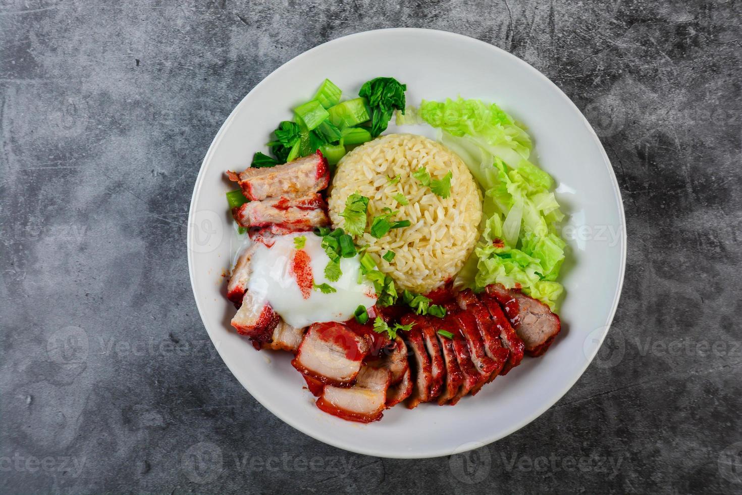 Barbecued red pork and crispy pork in red sauce, served with rice and vegetable on white plate. photo