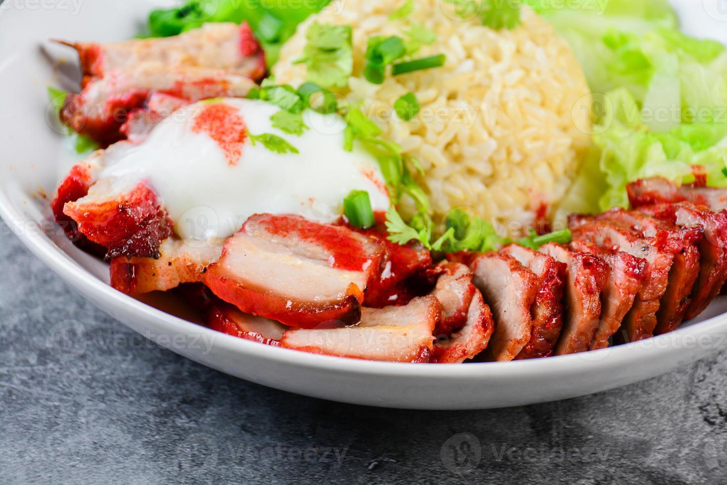 Barbecued red pork and crispy pork in red sauce, served with rice and vegetable on white plate. photo