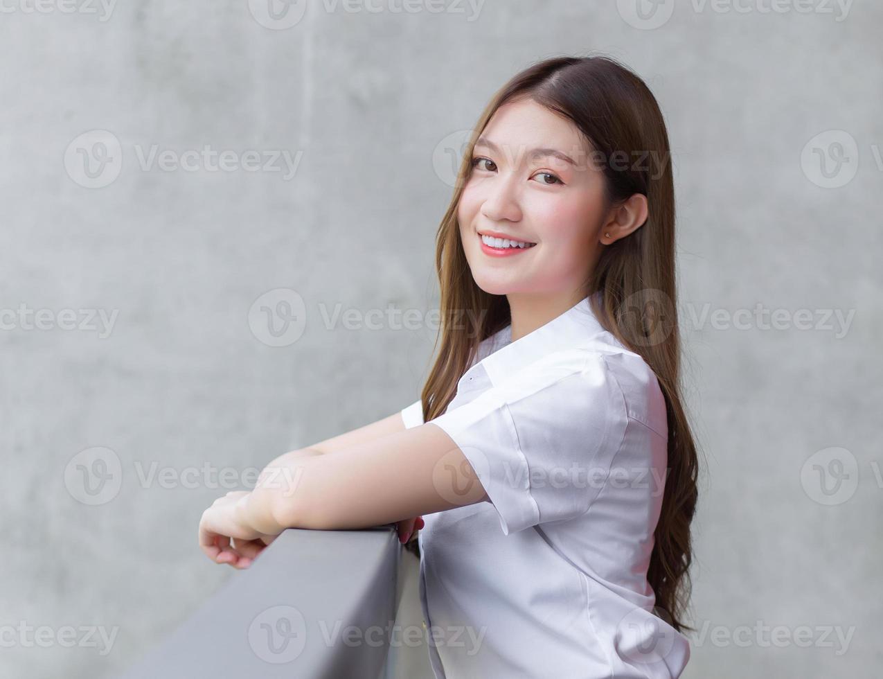 retrato de un estudiante tailandés adulto con uniforme de estudiante universitario. hermosa chica asiática sentada sonriendo felizmente en la universidad foto