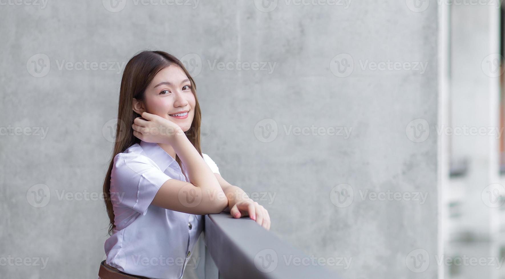 retrato de una estudiante tailandesa adulta con uniforme de estudiante universitario. hermosa chica asiática sentada sonriendo felizmente en la universidad. foto