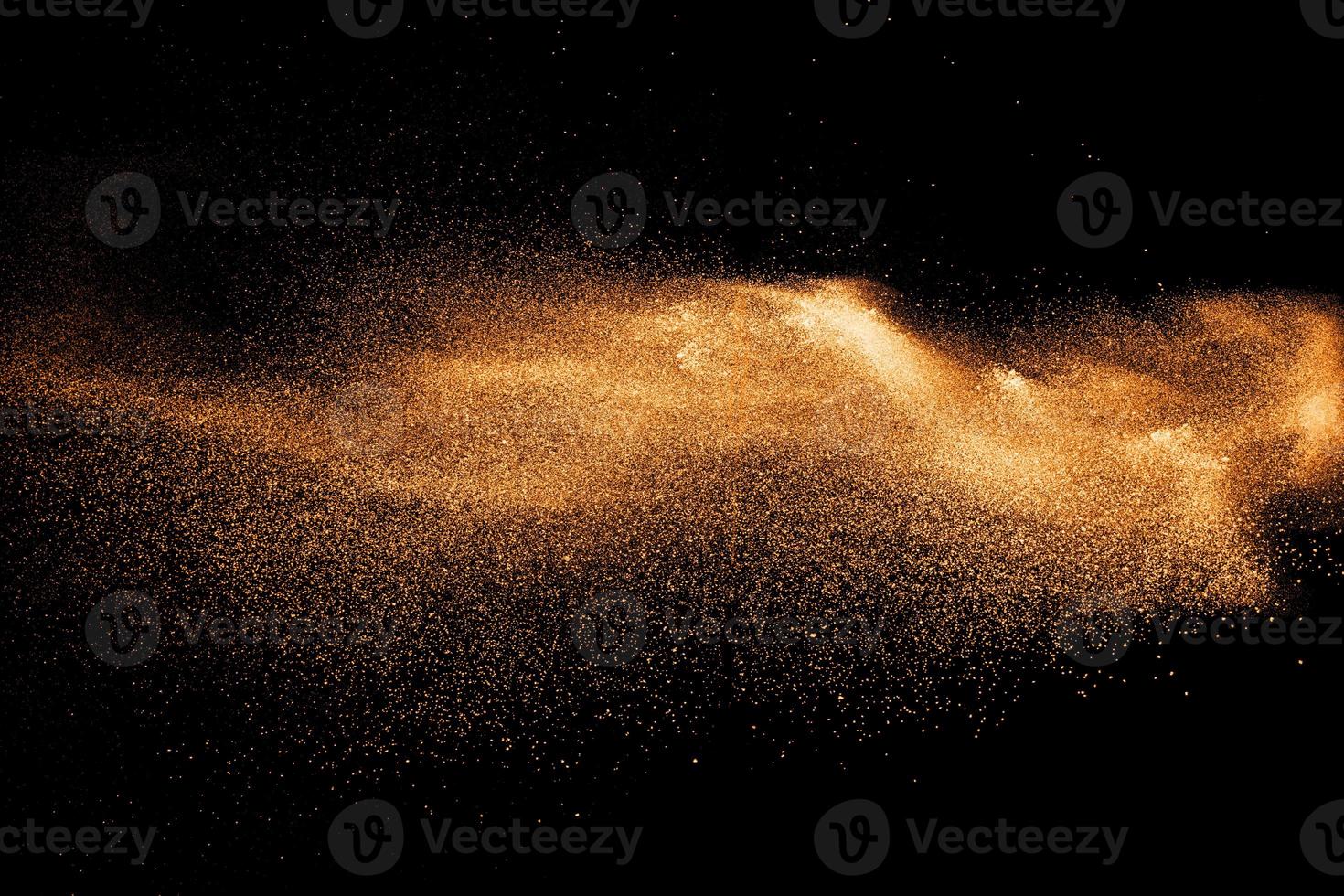 orange dust particles explosion on black background. Color powder dust splash. photo